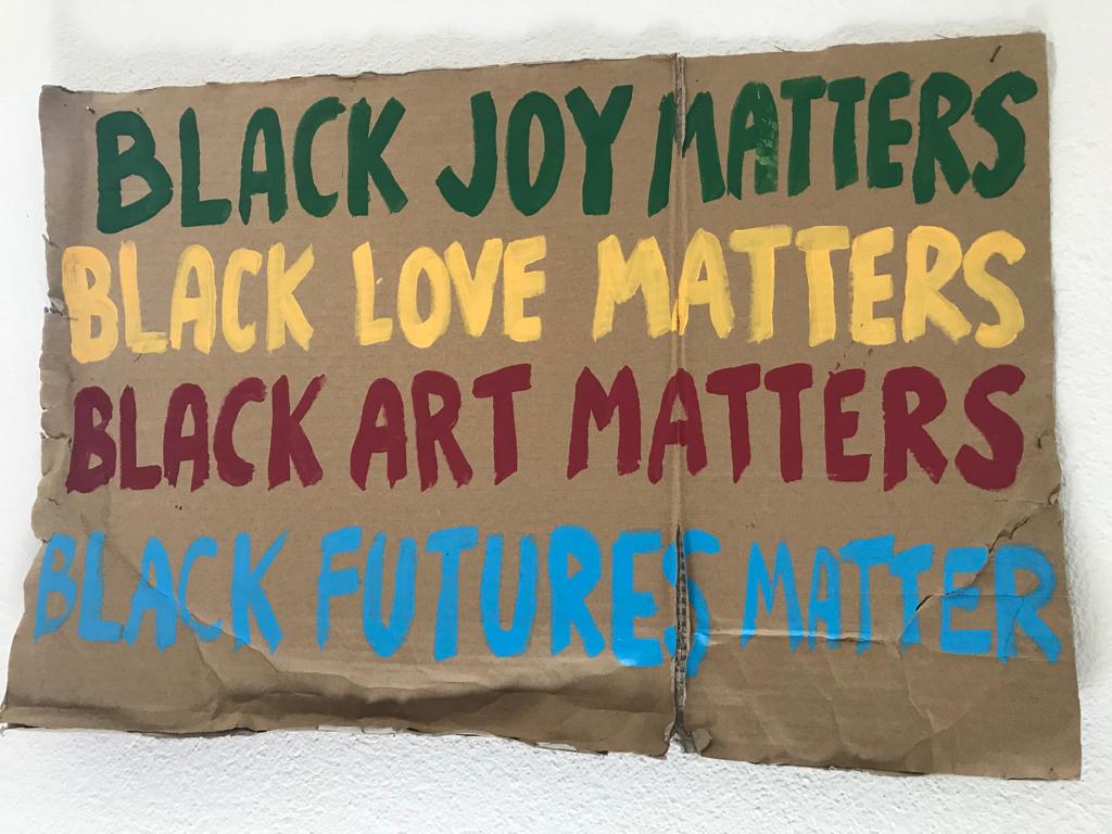 A cardbord sign that says: Black joy matters. Black love matters. Black art m atters. Black futures matter.