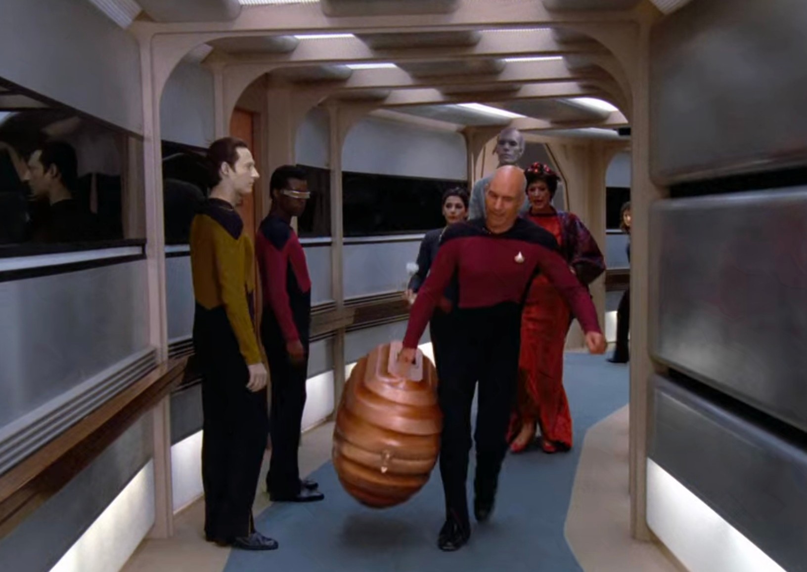 Captain Picard carries a big, futuristic suitcase through the hallway of the starship Enterprisedic